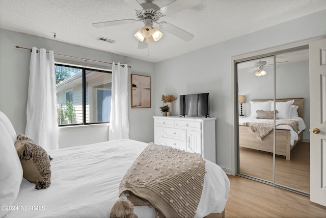 bedroom with a textured ceiling, light hardwood / wood-style floors, ceiling fan, and a closet