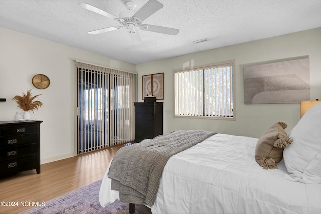 bedroom with wood-type flooring, a textured ceiling, multiple windows, and ceiling fan