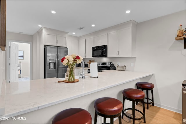 kitchen with light hardwood / wood-style floors, white cabinets, kitchen peninsula, a kitchen bar, and stainless steel appliances