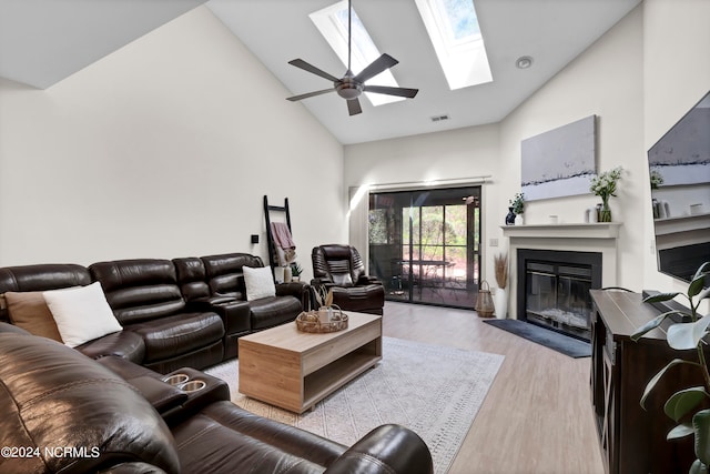 living room with light hardwood / wood-style flooring, ceiling fan, a skylight, and high vaulted ceiling