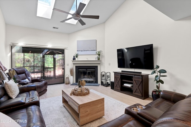 living room featuring ceiling fan, a skylight, light wood-type flooring, and high vaulted ceiling