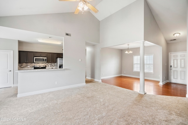 unfurnished living room featuring high vaulted ceiling, ceiling fan with notable chandelier, ornate columns, and carpet flooring