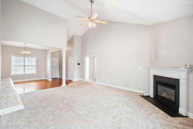 unfurnished living room featuring carpet floors, ceiling fan with notable chandelier, and high vaulted ceiling