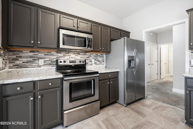 kitchen featuring dark brown cabinets, light stone countertops, tasteful backsplash, and stainless steel appliances