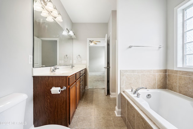 bathroom with tile patterned flooring, double sink vanity, tiled tub, toilet, and ceiling fan