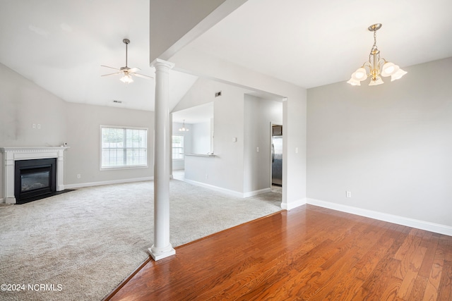 unfurnished living room featuring decorative columns, carpet, ceiling fan with notable chandelier, and vaulted ceiling