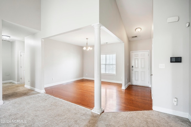 carpeted foyer featuring ornate columns, high vaulted ceiling, and an inviting chandelier