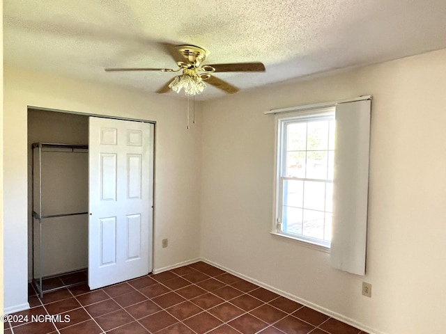 unfurnished bedroom featuring a closet, dark tile patterned floors, a textured ceiling, and ceiling fan