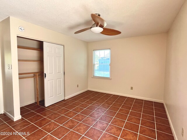 unfurnished bedroom with a closet, dark tile patterned floors, a textured ceiling, and ceiling fan