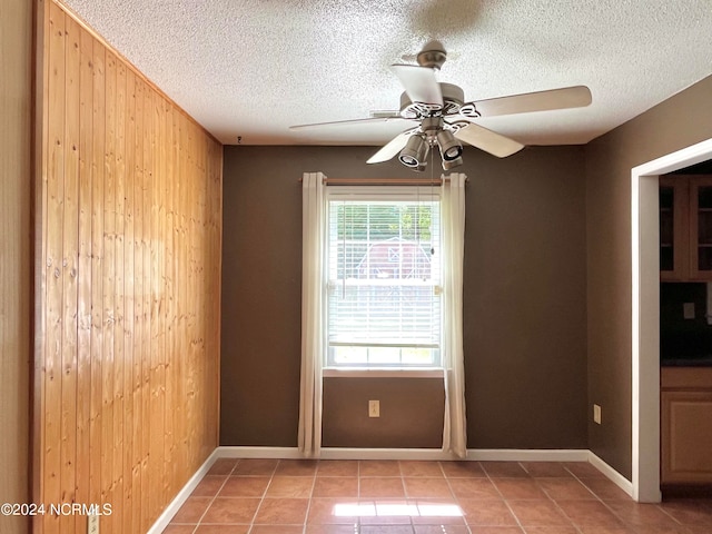 spare room with light tile patterned flooring, ceiling fan, wooden walls, and a textured ceiling