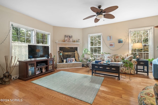 living room with a ceiling fan, a premium fireplace, and wood finished floors