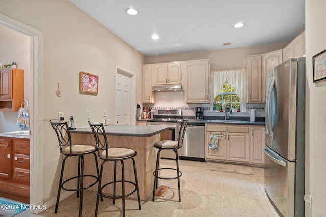 kitchen featuring dark countertops, a kitchen breakfast bar, stainless steel appliances, under cabinet range hood, and a sink