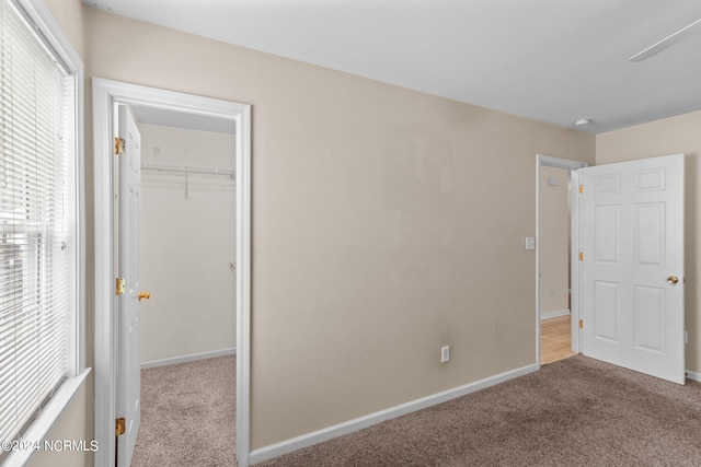 unfurnished bedroom featuring a closet, a spacious closet, and light colored carpet