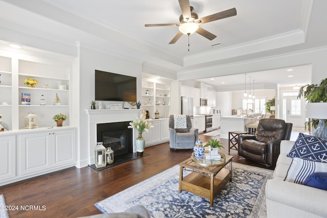 living room featuring built in features, a tray ceiling, dark wood-style flooring, and ornamental molding