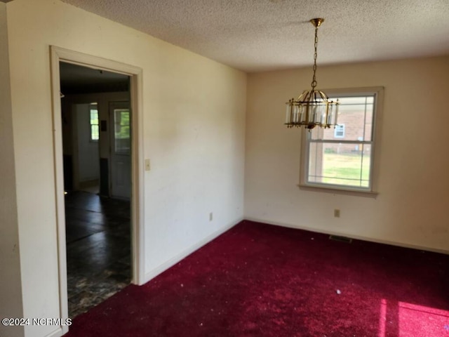 carpeted empty room featuring an inviting chandelier and a textured ceiling