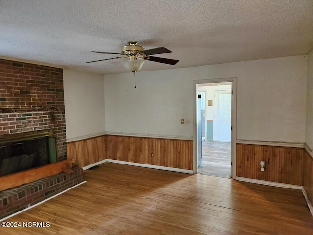 unfurnished living room featuring ceiling fan, wood-type flooring, a brick fireplace, and a textured ceiling