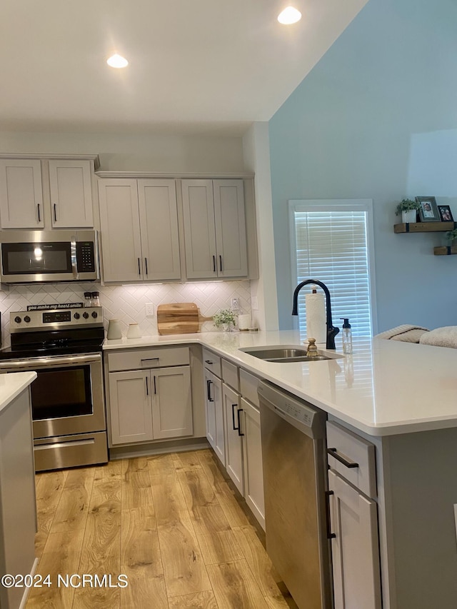 kitchen featuring a sink, light countertops, appliances with stainless steel finishes, light wood finished floors, and tasteful backsplash