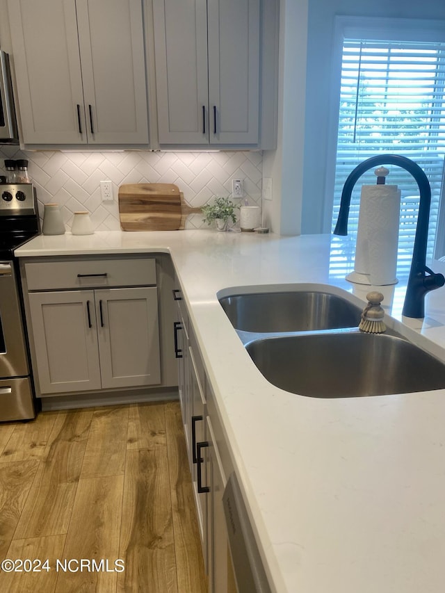 kitchen featuring electric stove, gray cabinets, light countertops, a sink, and light wood-type flooring