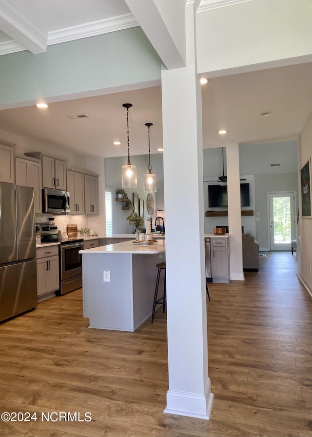 kitchen featuring stainless steel appliances, wood finished floors, open floor plan, hanging light fixtures, and light countertops