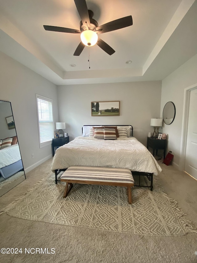 carpeted bedroom featuring ceiling fan, a tray ceiling, and baseboards