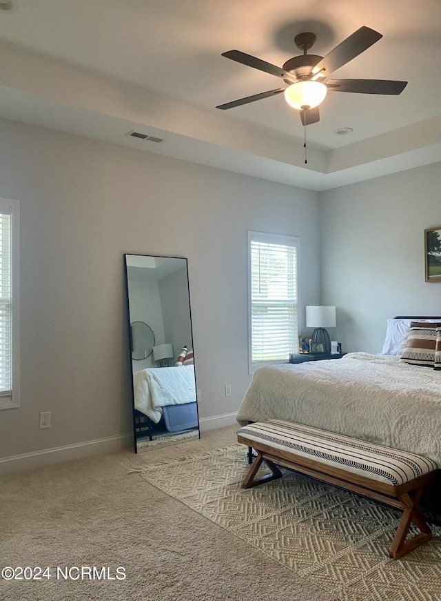 carpeted bedroom featuring a ceiling fan, baseboards, visible vents, and a tray ceiling