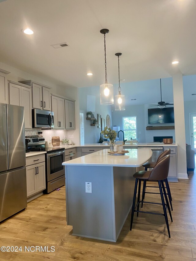 kitchen featuring decorative backsplash, stainless steel appliances, a breakfast bar, a center island, and light wood-type flooring