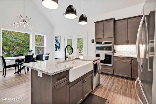 kitchen with appliances with stainless steel finishes, pendant lighting, tasteful backsplash, sink, and light stone countertops