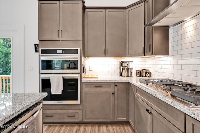 kitchen featuring light stone countertops, appliances with stainless steel finishes, wall chimney range hood, and light hardwood / wood-style floors