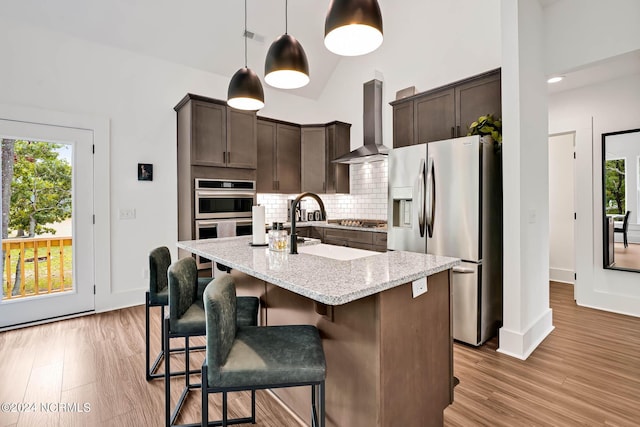 kitchen with dark brown cabinetry, wall chimney range hood, decorative light fixtures, and stainless steel appliances