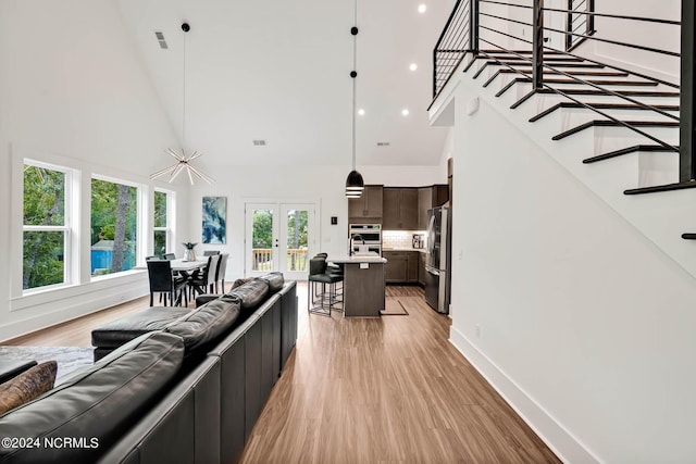 living room featuring a towering ceiling, light wood-type flooring, and french doors