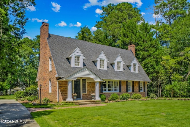 new england style home with roof with shingles, a front lawn, a chimney, and brick siding