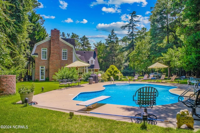 view of pool with a patio, a lawn, and a diving board