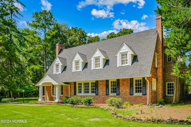 new england style home with roof with shingles, brick siding, a chimney, and a front lawn