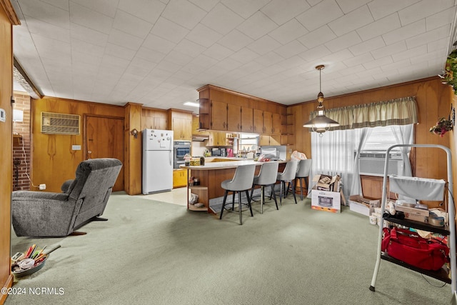 kitchen with a kitchen bar, white refrigerator, hanging light fixtures, light colored carpet, and kitchen peninsula