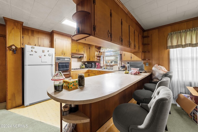 kitchen with wood walls, crown molding, white refrigerator, kitchen peninsula, and oven