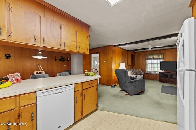 kitchen featuring light colored carpet, hanging light fixtures, wooden walls, kitchen peninsula, and white appliances