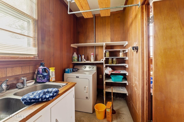 clothes washing area with sink, washer / dryer, cabinets, and wood walls