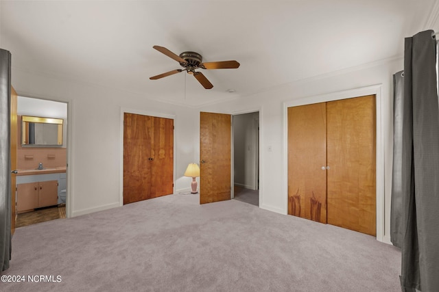 unfurnished bedroom featuring ensuite bathroom, sink, light carpet, two closets, and ceiling fan