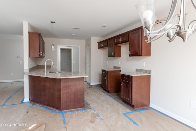 kitchen featuring sink, dark brown cabinets, light stone countertops, decorative light fixtures, and kitchen peninsula