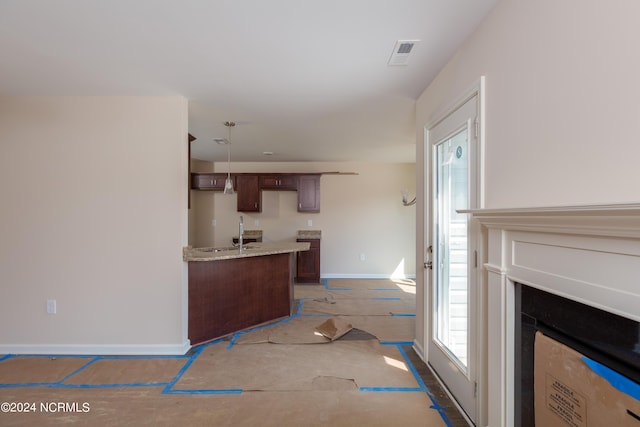 kitchen with pendant lighting, light stone countertops, sink, and dark brown cabinets