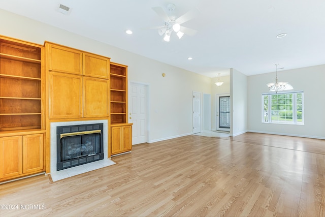 unfurnished living room with ceiling fan with notable chandelier, a tiled fireplace, and light hardwood / wood-style floors