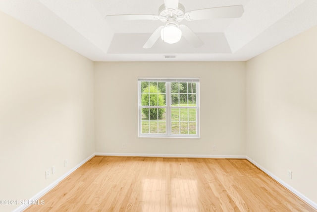 spare room featuring a tray ceiling, ceiling fan, and light wood-type flooring