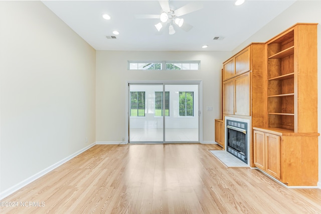 unfurnished living room featuring a tile fireplace, ceiling fan, and light hardwood / wood-style floors