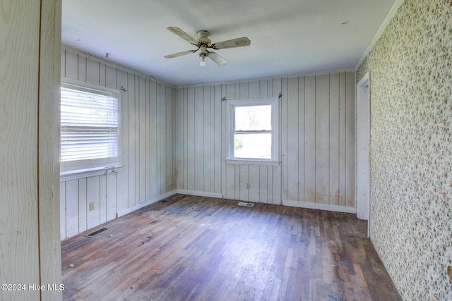 unfurnished room with wood walls, a wealth of natural light, dark wood-type flooring, and ceiling fan