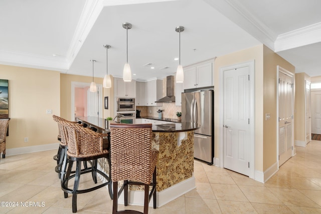 kitchen with wall chimney range hood, white cabinetry, stainless steel appliances, a kitchen bar, and decorative light fixtures