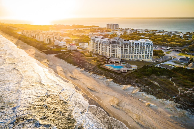 aerial view at dusk featuring a water view and a beach view