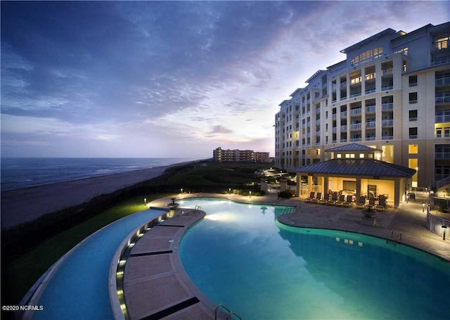 pool at dusk with a gazebo, a patio area, and a water view