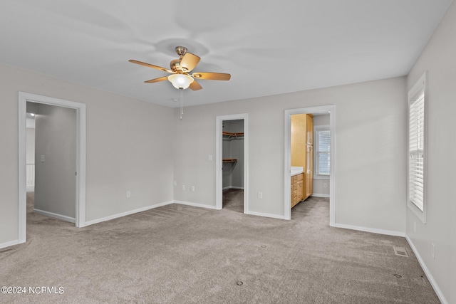 unfurnished bedroom featuring ceiling fan, connected bathroom, a walk in closet, a closet, and light carpet