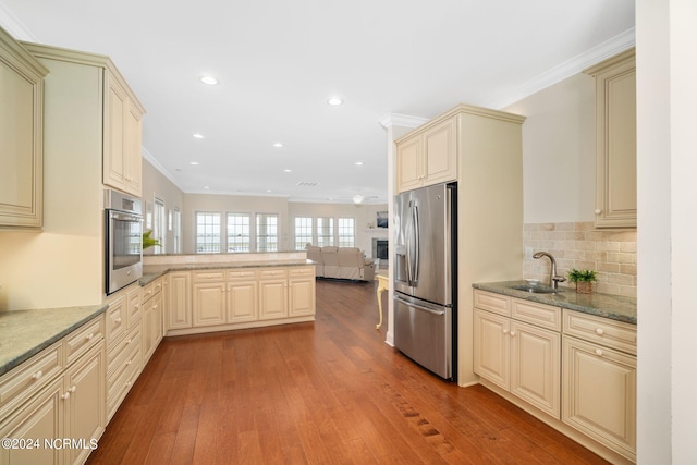 kitchen featuring sink, dark stone countertops, stainless steel appliances, cream cabinets, and light wood-type flooring