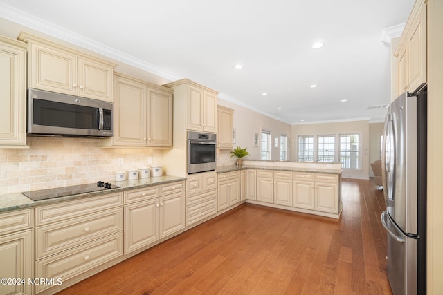 kitchen with ornamental molding, appliances with stainless steel finishes, kitchen peninsula, light hardwood / wood-style floors, and cream cabinetry